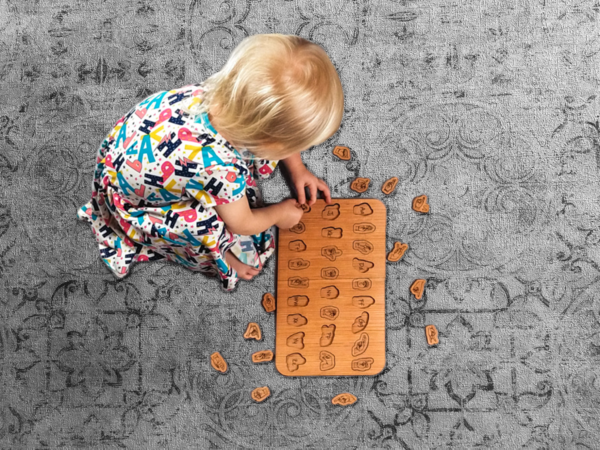 Little girl playing with a wooden ASL Alphabet puzzle on the floor.