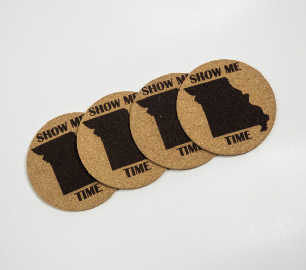 Four cork coasters, engraved with the state of Missouri shape and the words "Show me time". The coasters are laid out in a diagonal line.