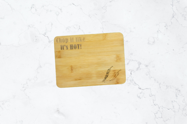 Small Bamboo cutting board, engraved with the words "Chop it like it's hot" in the top-left corner, and 2 chili peppers in the bottom-right, one is chopped.