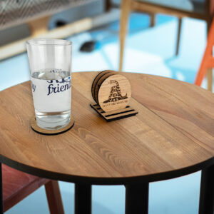 Set of wooden coasters on a table. 3 in a stand and one under a glass of water. Visible coaster engraved with "Don't tread on me" text and snake.