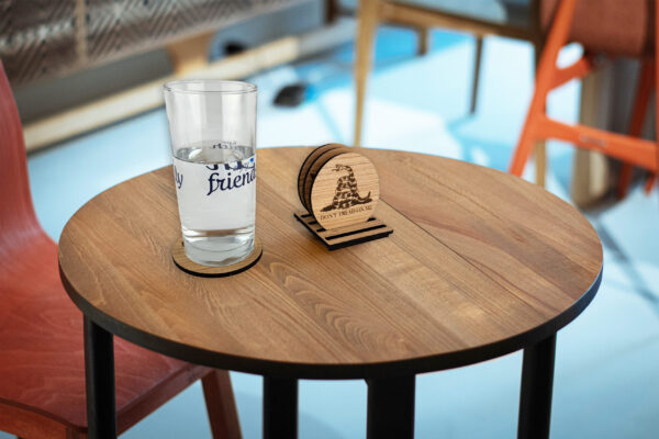 Set of wooden coasters on a table. 3 in a stand and one under a glass of water. Visible coaster engraved with "Don't tread on me" text and snake.