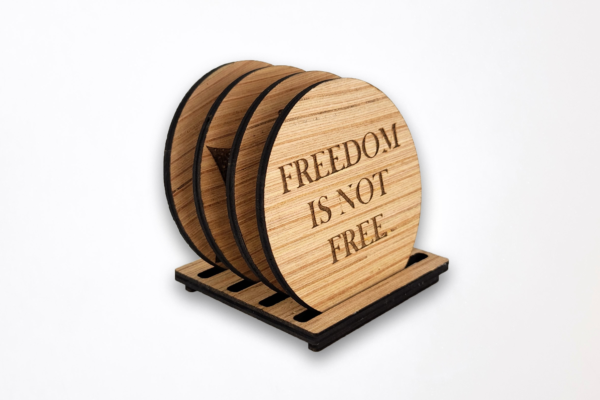 Wooden coaster set in stand, front coaster is engraved with the words "Freedom is not free"