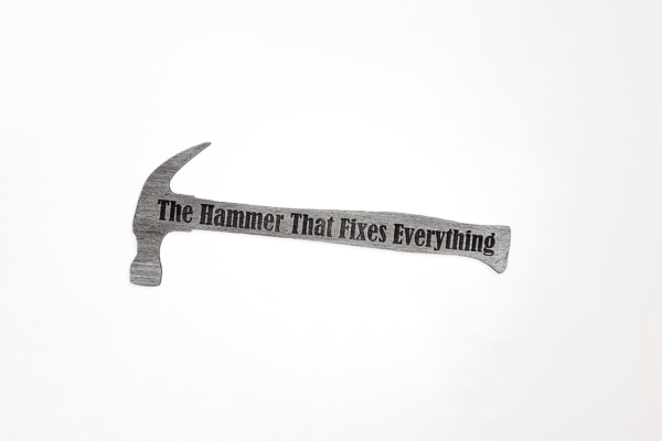 Wooden hammer shape that is painted silver and engraved with the words "The Hammer That Fixes Everything"