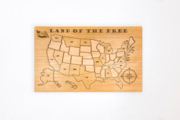 Wooden United States map puzzle, with the words "Land of the free" across the top and a graphic of a bald eagle in front of the American flag in the top left corner. Some state pieces are removed from frame.