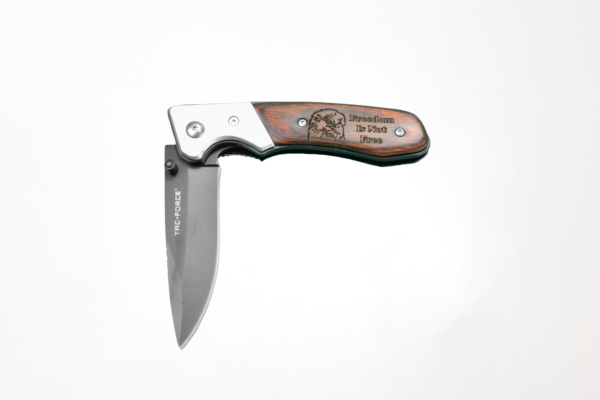 Tac-force pocket knife lying half-open on a white background. The wooden handle is engraved with the head of a bald eagle and the words "Freedom is not free"