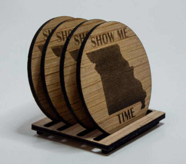 Four wooden coasters, engraved with the state of Missouri shape and the words "Show me time". The coasters are on a stand.