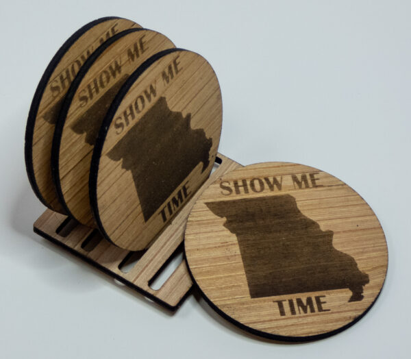 Four wooden coasters, engraved with the state of Missouri shape and the words "Show me time". Three coasters are on the stand, the fourth is laid against the front of the stand.