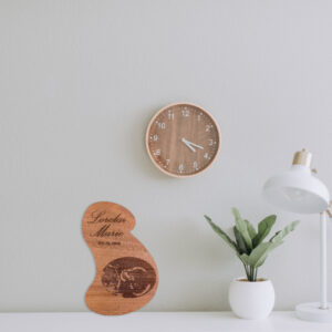 Stylized pregnant bust shaped wooden plaque engraved with a sonogram image, name and date, standing on a desk.