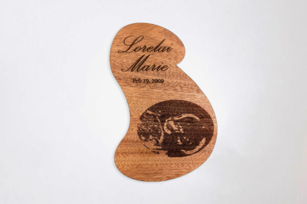 Stylized pregnant bust shaped wooden plaque engraved with a sonogram image, name, and date, on a white background