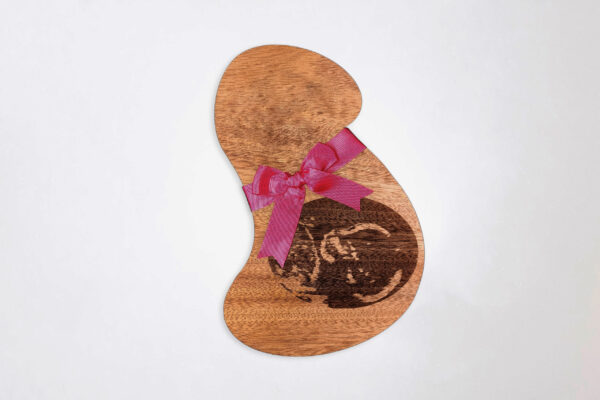 Stylized pregnant bust shaped wooden plaque, engraved with an ultrasound image and tied with a pink ribbon, on a white background.