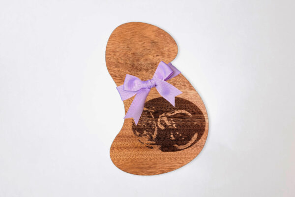 Stylized pregnant bust shaped wooden plaque, engraved with an ultrasound image and tied with a purple ribbon, on a white background.