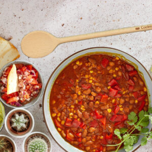 Wood spoon with the words "Cookin' with gas" engraved on the handle laying next to a bowl of chili