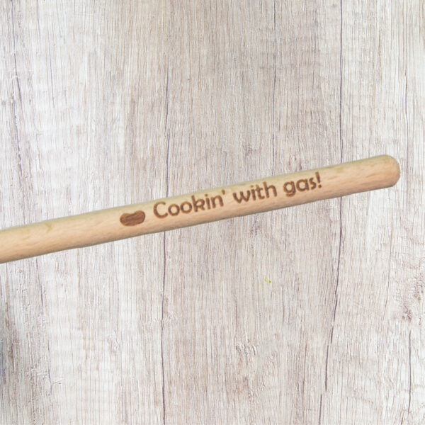 Handle of a wood spoon engraved with the words "Cookin' with gas" and a bean shape