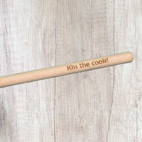 Handle of a wood spoon engraved with the words "Kiss the cook"