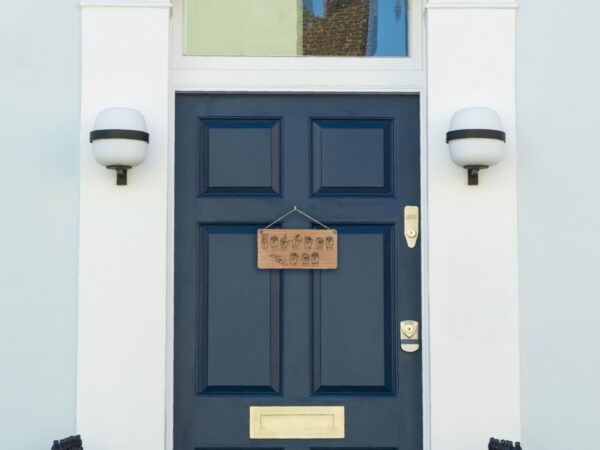 Wooden sign laser engraved with ASL handshapes, fingerspelling: Welcome home. Sign is hung on a blue door.