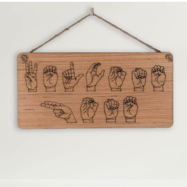 Closeup of a wooden sign laser engraved with ASL handshapes, fingerspelling: Welcome home. Sign is hung on a white background.