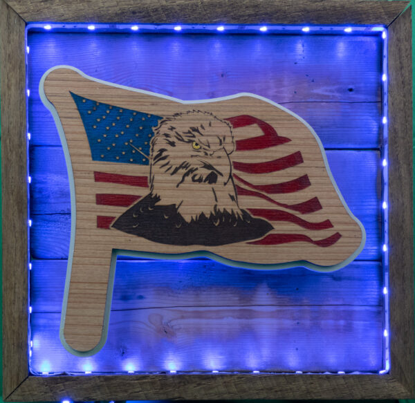 Layered edge-lit lightbox with a bald eagle head in front of the American flag. Rustic wood backer and frame. Lit with blue LED lights.