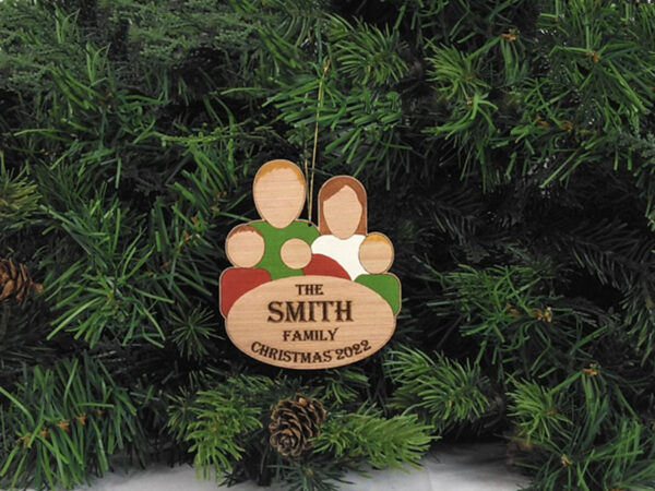 Painted, wooden family group ornament hanging on pine boughs. Ornament features five characters and the words: The Smith Family, Christmas 2022