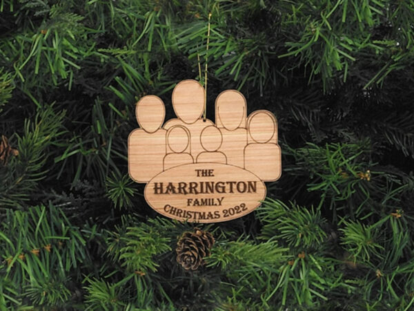 Unpainted, wooden family group ornament hanging on pine boughs. Ornament features six characters and the words: The Harrington Family, Christmas 2022