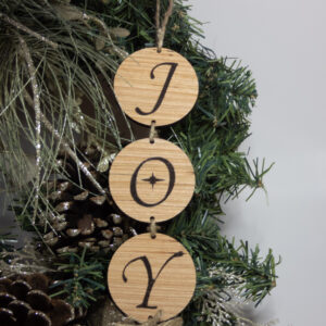 3-tiered wood round sign. Each round features a letter to spell out the word "Joy" the O has a stylized star in the middle. The sign is hung on pine boughs.