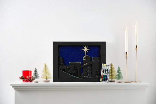 Beautiful 3d lightbox featuring a simple nativity scene with a remote leaned against the corner. Lightbox is displayed on a mantle.