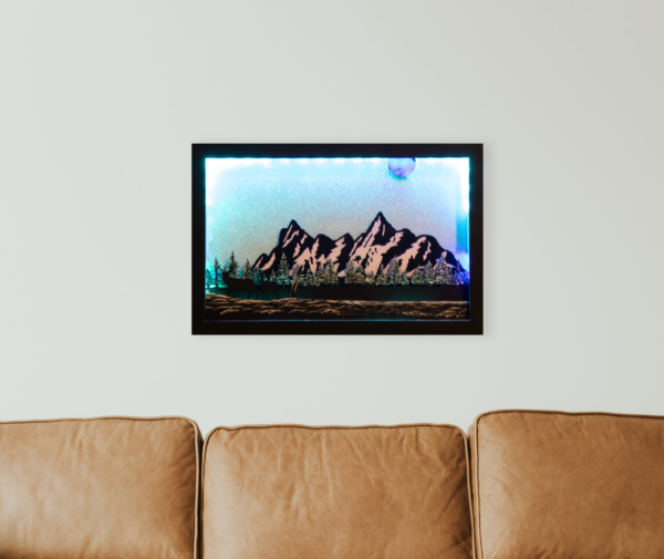 Beautiful 3d lightbox featuring a snowy mountain scene with a glittery white background reflecting the soft blue light through the scene. Lightbox is hanging on a wall above a sofa.