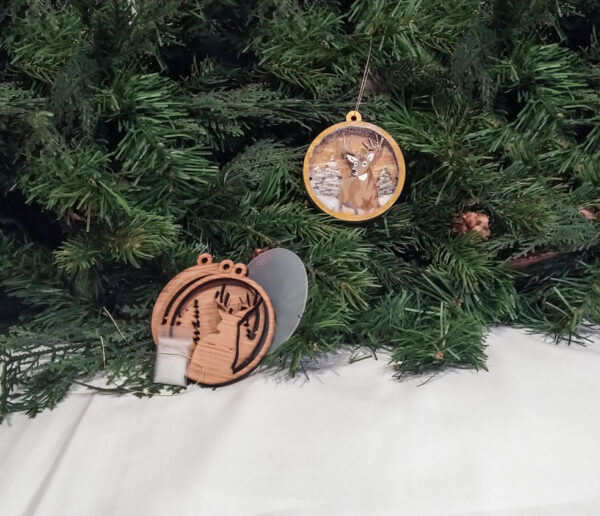 finished deer Christmas snow globe ornament hanging on pine boughs. Ornament kit is sitting next to it.