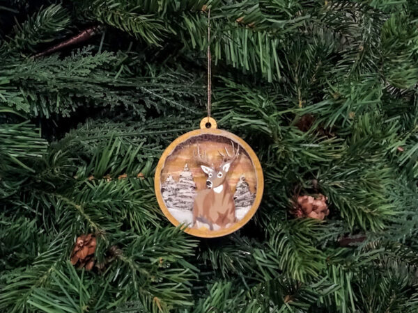 Finished deer Christmas snow globe ornament hanging on pine boughs.