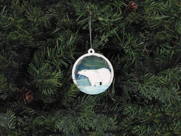 Finished polar bear Christmas snow globe ornament hanging on pine boughs.