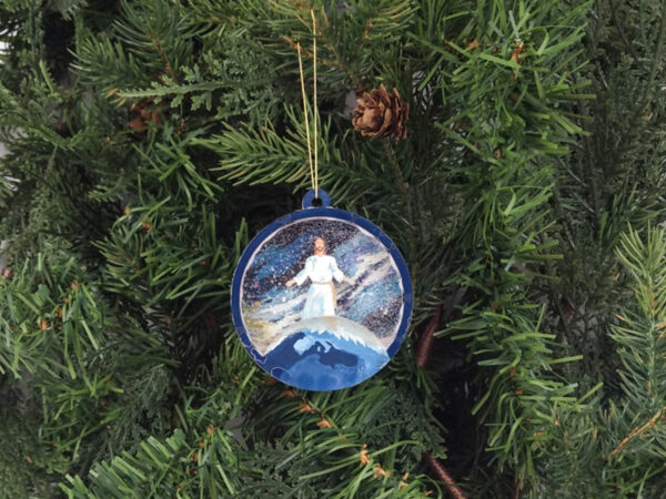 Finished Jesus Christmas snow globe ornament hanging on pine boughs.