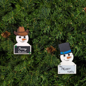 Painted classic and cowboy snowman ornaments hung on pine boughs.