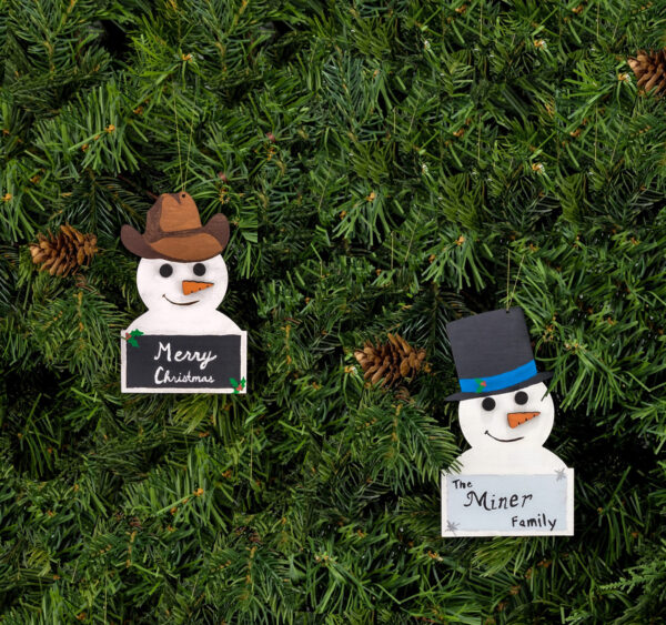 Painted classic and cowboy snowman ornaments hung on pine boughs.