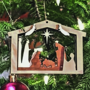 Layered 3D Nativity Christmas tree ornament, featuring the holy family in a stable, with wise men, shepherd, angels, and star. Ornament is hanging on a Christmas tree.