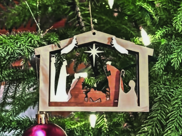 Layered 3D Nativity Christmas tree ornament, featuring the holy family in a stable, with wise men, shepherd, angels, and star. Ornament is hanging on a Christmas tree.