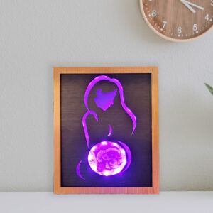 Framed LED lightbox with stylized line silhouette of a woman, the belly displays an ultrasound image engraved on acrylic. Lightbox is illuminated with bright purple light and displayed on a shelf.