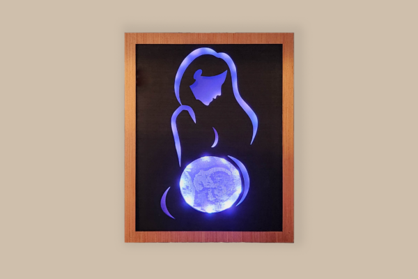 Framed LED lightbox with stylized line silhouette of a woman, the belly displays an ultrasound image engraved on acrylic. Lightbox is illuminated with soft blue light and displayed on a wall.