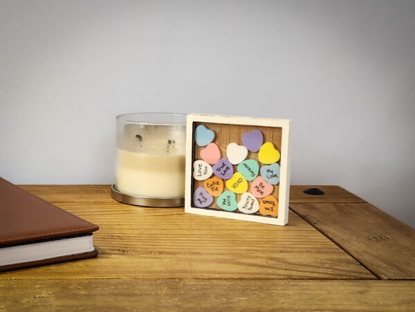 White sweetheart frame with an acrylic face, filled with colorful acrylic hearts. Most have messages written on them, the top few are blank.